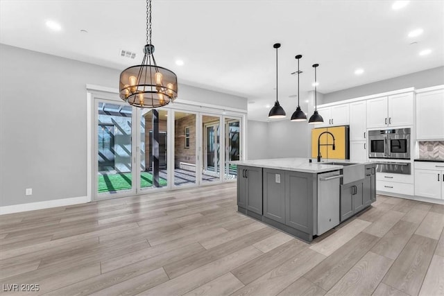 kitchen featuring pendant lighting, an island with sink, an inviting chandelier, gray cabinets, and white cabinetry