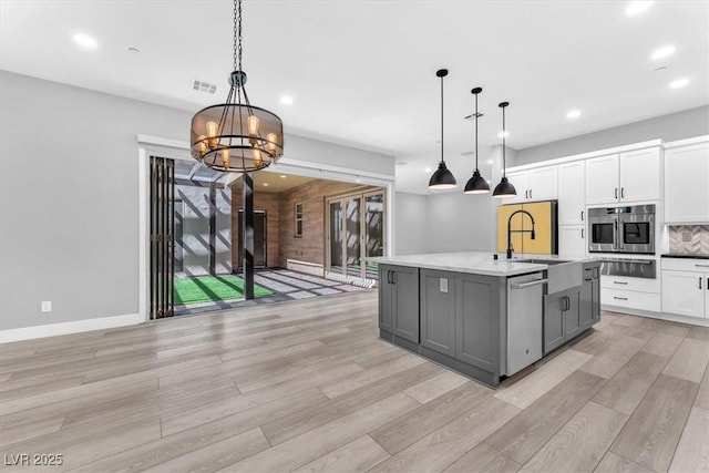 kitchen with hanging light fixtures, a notable chandelier, a kitchen island with sink, gray cabinetry, and white cabinetry