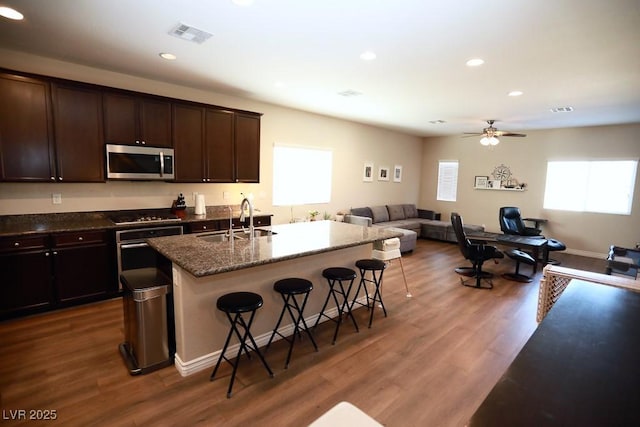 kitchen with sink, dark wood-type flooring, an island with sink, a kitchen bar, and appliances with stainless steel finishes