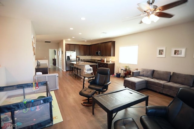 living room with ceiling fan, light wood-type flooring, and sink