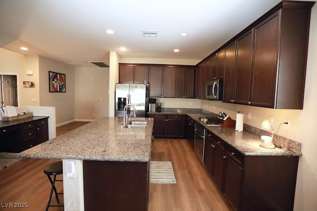 kitchen featuring stainless steel appliances, light stone counters, a center island with sink, and sink