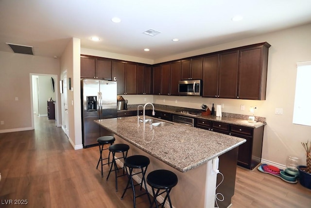 kitchen with a breakfast bar, stainless steel appliances, a kitchen island with sink, and sink