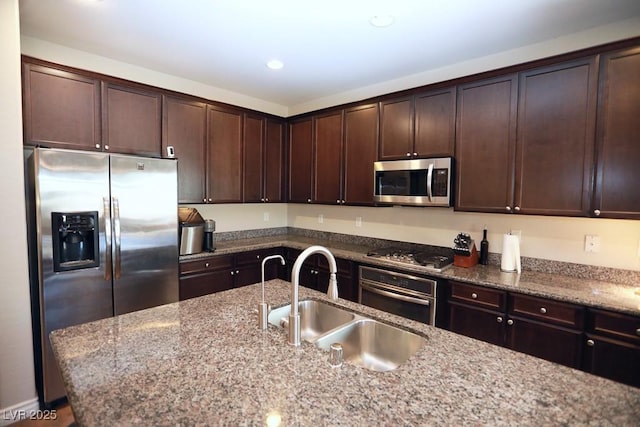 kitchen featuring appliances with stainless steel finishes, dark brown cabinetry, light stone counters, and sink