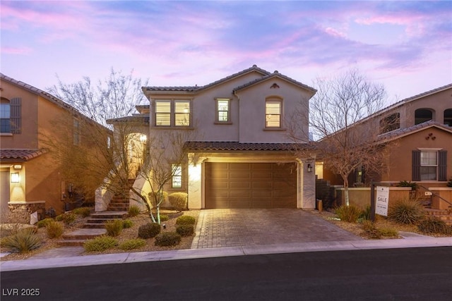 mediterranean / spanish-style home with an attached garage, stucco siding, driveway, and a tiled roof