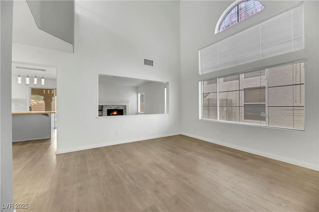 unfurnished living room with light hardwood / wood-style floors, a towering ceiling, and a wealth of natural light