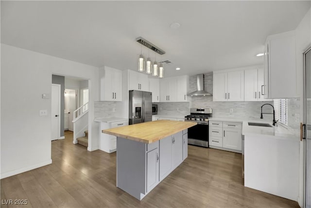 kitchen with wood counters, a center island, wall chimney range hood, white cabinetry, and stainless steel appliances