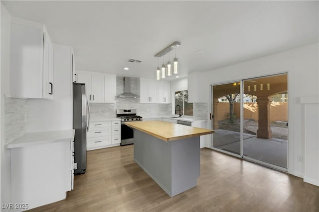 kitchen with white cabinets, a kitchen island, wall chimney range hood, and appliances with stainless steel finishes