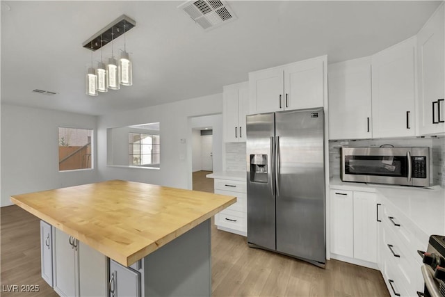 kitchen with wood counters, a center island, white cabinets, decorative light fixtures, and stainless steel appliances