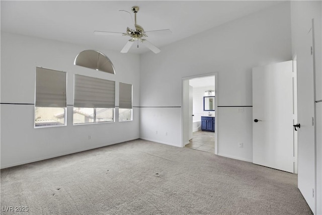 unfurnished bedroom featuring light carpet, a high ceiling, connected bathroom, and ceiling fan