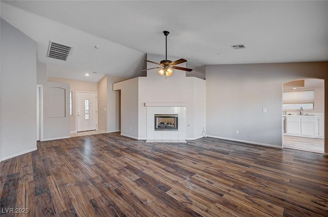 unfurnished living room with ceiling fan, sink, dark hardwood / wood-style flooring, lofted ceiling, and a tiled fireplace