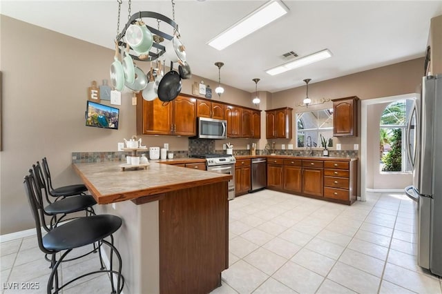 kitchen with backsplash, kitchen peninsula, a breakfast bar area, light tile patterned floors, and appliances with stainless steel finishes