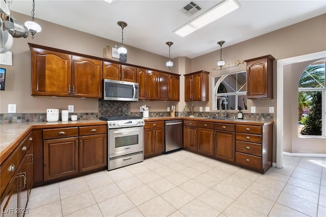 kitchen with decorative backsplash, appliances with stainless steel finishes, sink, light tile patterned floors, and pendant lighting