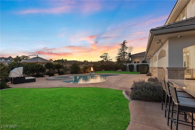 pool at dusk featuring an in ground hot tub, a yard, exterior bar, and a patio area