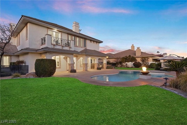 back house at dusk with a yard, a balcony, a patio, and a fenced in pool