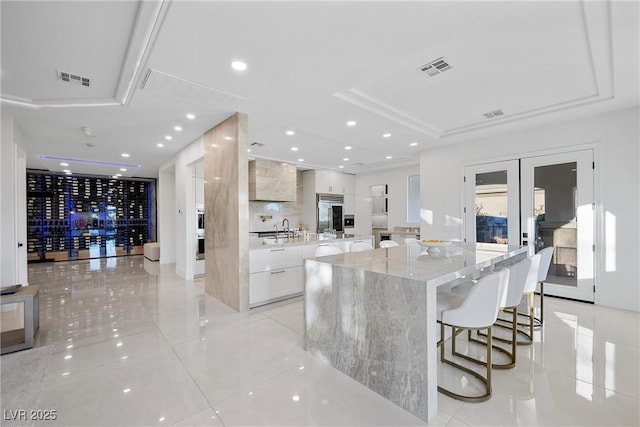 kitchen featuring white cabinetry, a center island, light stone countertops, a breakfast bar area, and light tile patterned flooring