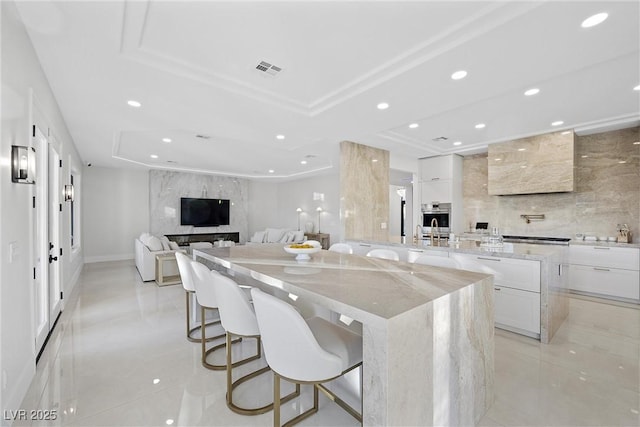 kitchen with a kitchen breakfast bar, a spacious island, light stone countertops, a tray ceiling, and white cabinetry