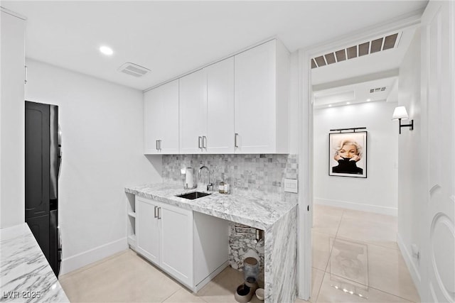 kitchen with light stone countertops, decorative backsplash, black fridge, sink, and white cabinetry