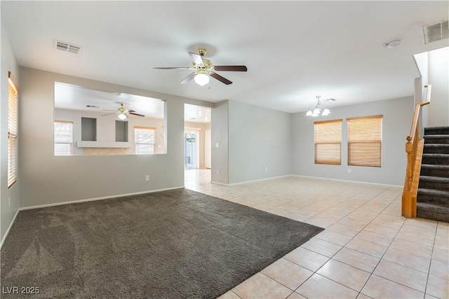 tiled empty room featuring ceiling fan with notable chandelier