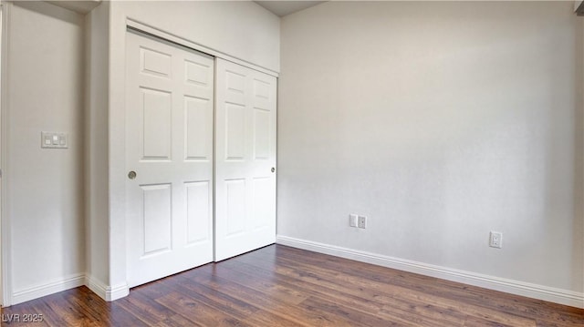 unfurnished bedroom featuring dark wood-style floors, a closet, and baseboards