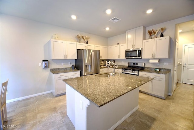 kitchen featuring stainless steel appliances, sink, stone counters, white cabinetry, and an island with sink