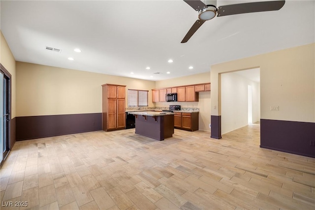 kitchen featuring black appliances, a kitchen breakfast bar, a center island, and light wood-type flooring