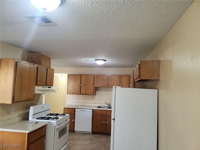 kitchen with a textured ceiling, light tile patterned flooring, white appliances, and sink