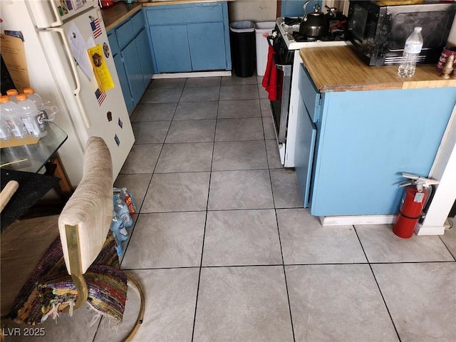 kitchen with dark tile patterned floors, white appliances, and blue cabinetry