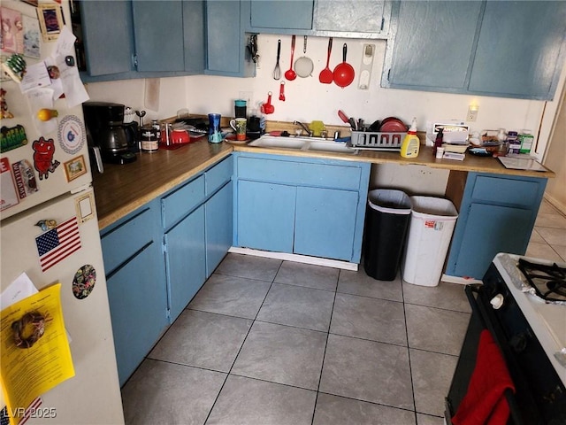 kitchen featuring black range with gas cooktop, sink, blue cabinetry, white refrigerator, and dark tile patterned flooring