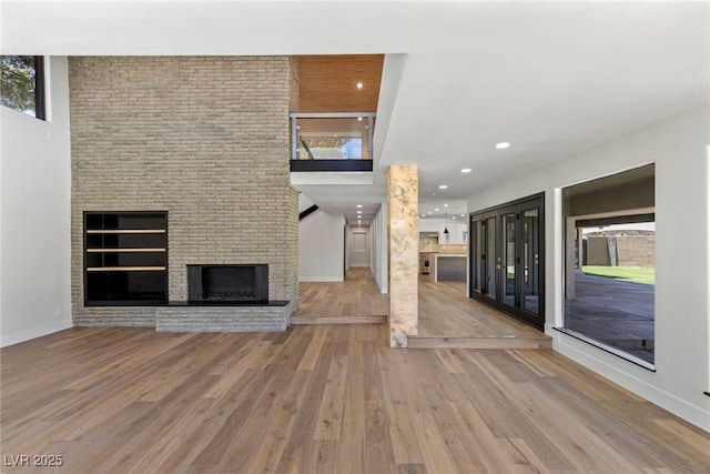 unfurnished living room with a brick fireplace, a towering ceiling, and hardwood / wood-style floors