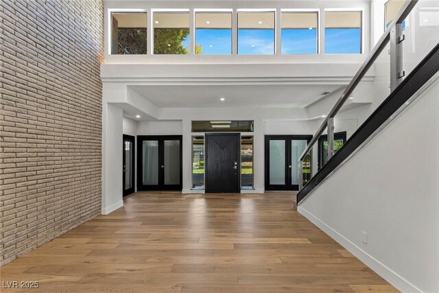 foyer with french doors, brick wall, light wood-type flooring, and a high ceiling