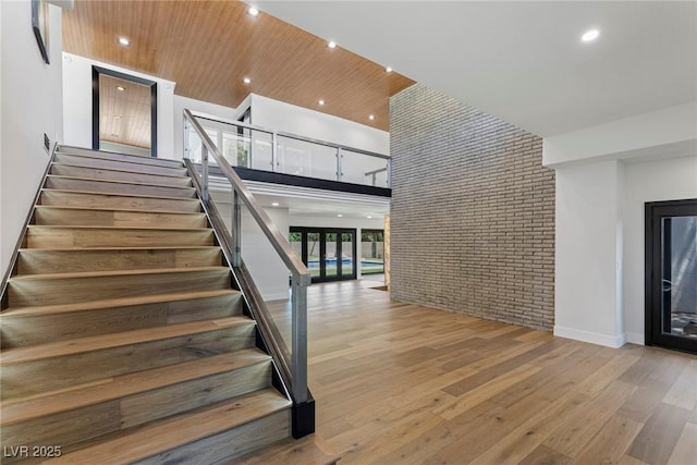 stairway with french doors, wood ceiling, a towering ceiling, brick wall, and hardwood / wood-style floors