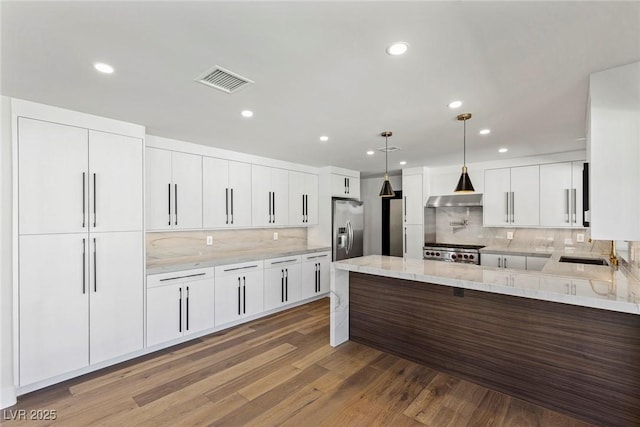 kitchen with white cabinetry, wood-type flooring, hanging light fixtures, stainless steel refrigerator with ice dispenser, and light stone countertops