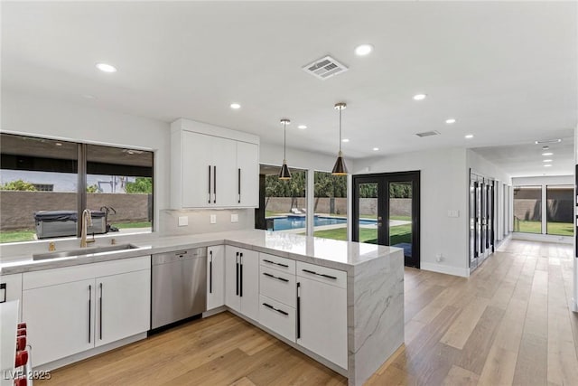 kitchen featuring sink, white cabinetry, decorative light fixtures, stainless steel dishwasher, and kitchen peninsula