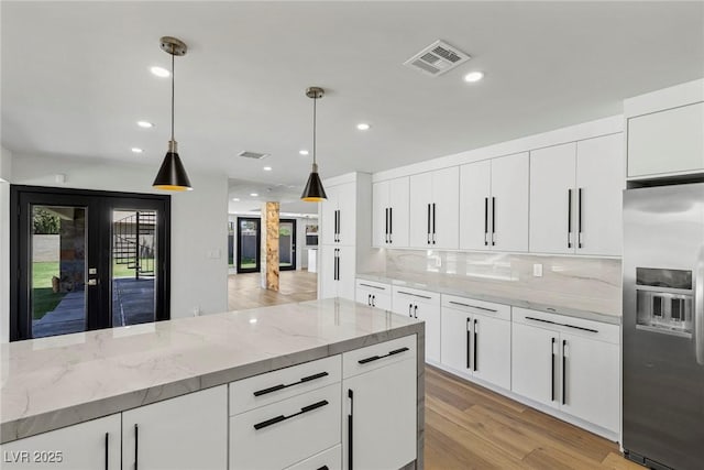 kitchen with stainless steel refrigerator with ice dispenser, light stone countertops, pendant lighting, and white cabinets