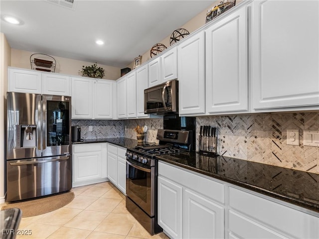 kitchen with white cabinetry, tasteful backsplash, dark stone counters, light tile patterned floors, and appliances with stainless steel finishes