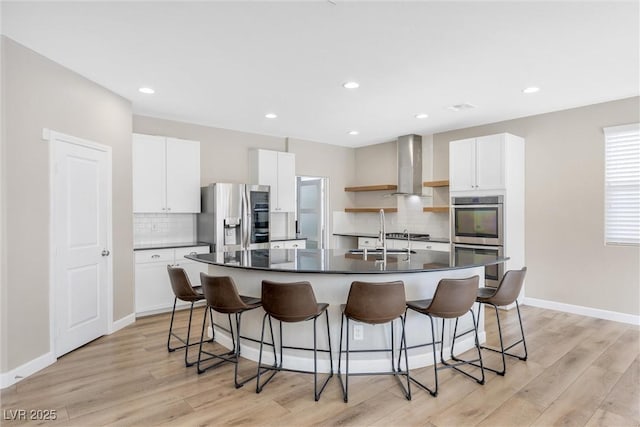 kitchen with a kitchen island with sink, white cabinets, wall chimney range hood, sink, and stainless steel appliances