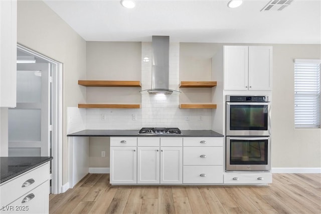 kitchen featuring wall chimney exhaust hood, light wood-type flooring, white cabinetry, and stainless steel appliances