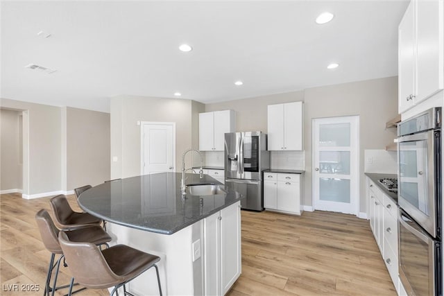 kitchen with decorative backsplash, stainless steel appliances, white cabinetry, and a kitchen island with sink