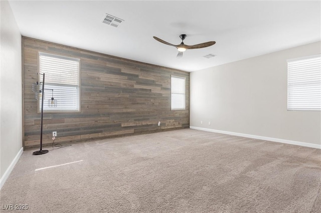 empty room featuring wooden walls, carpet floors, and ceiling fan