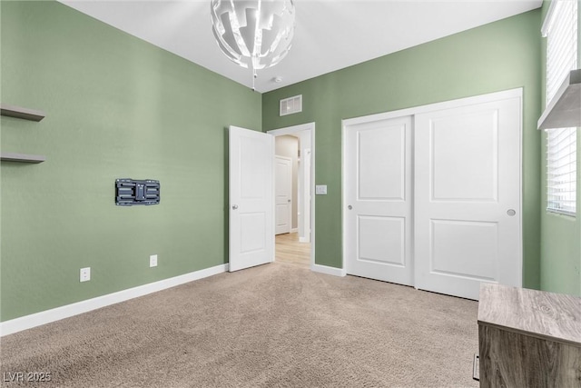 unfurnished bedroom with light colored carpet, a closet, and a notable chandelier