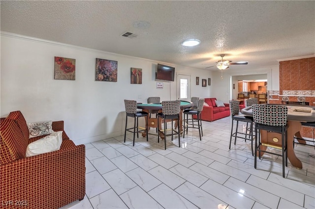 dining space with ceiling fan, ornamental molding, and a textured ceiling