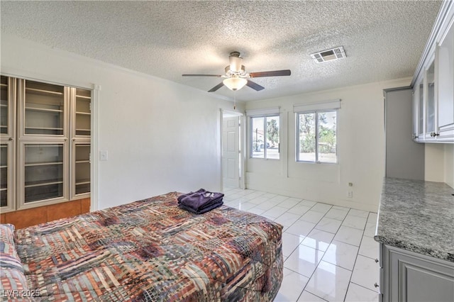 bedroom with ceiling fan, light tile patterned floors, a textured ceiling, and a closet