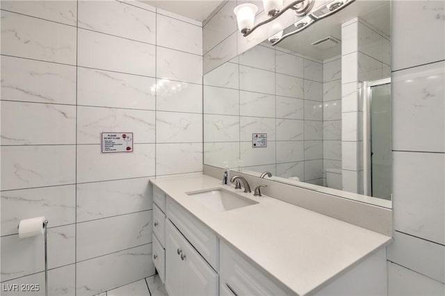 bathroom featuring an enclosed shower, vanity, and tile walls