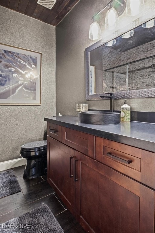 bathroom with toilet, visible vents, a textured wall, and vanity