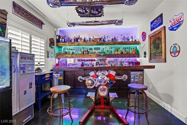 bar featuring finished concrete floors, baseboards, and wet bar