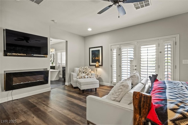 living room featuring a glass covered fireplace, baseboards, visible vents, ceiling fan, and wood finished floors