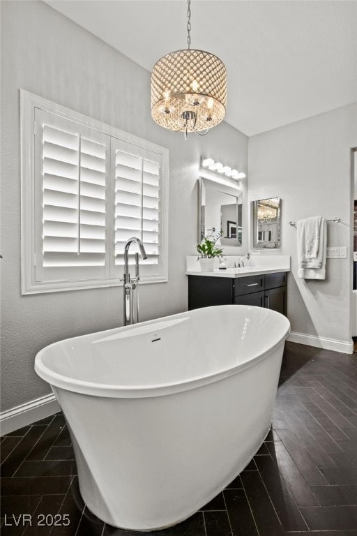 full bathroom featuring a freestanding tub, vanity, wood finished floors, baseboards, and a notable chandelier