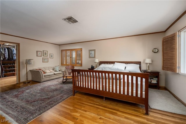 bedroom with multiple windows, a spacious closet, light hardwood / wood-style flooring, and ornamental molding