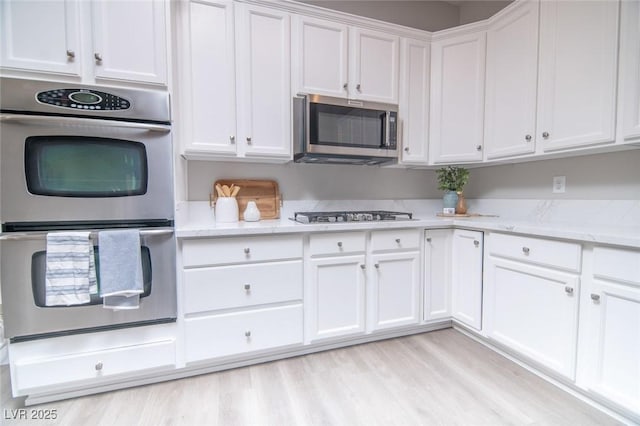 kitchen with light stone countertops, white cabinetry, stainless steel appliances, and light hardwood / wood-style flooring