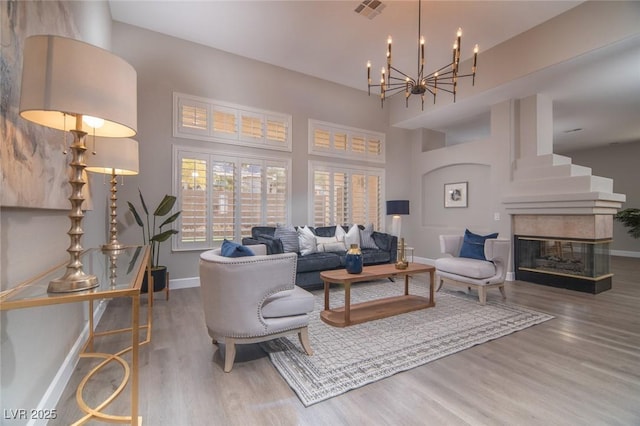 living room featuring a multi sided fireplace, wood-type flooring, a towering ceiling, and a chandelier